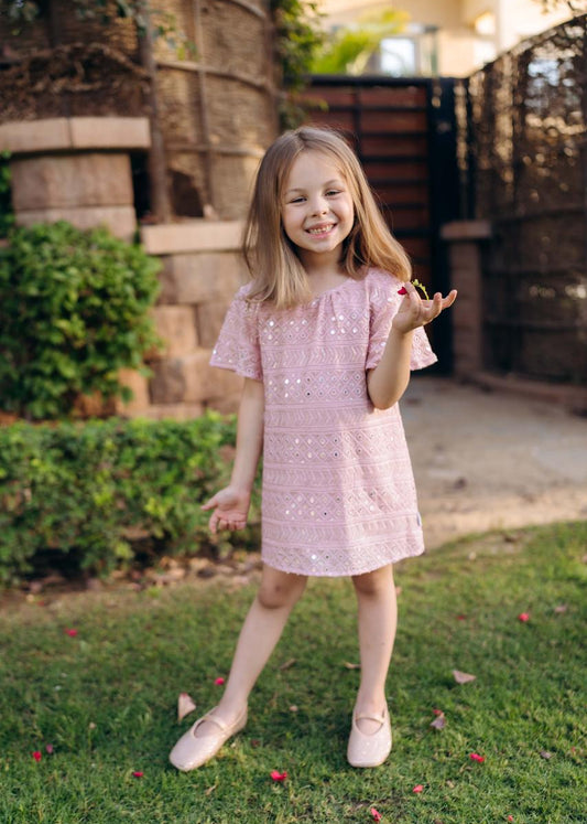 Young girl in a pink dress standing on grass with a building in the background.