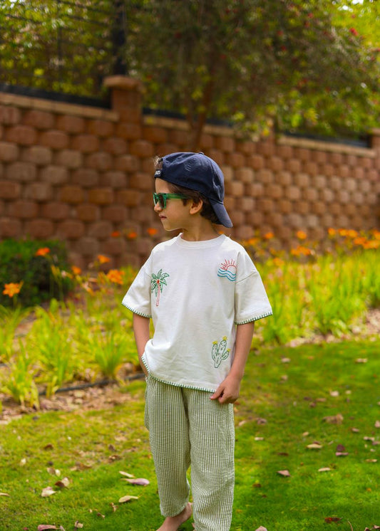 Child wearing a white shirt with graphics and green pants standing in a garden.