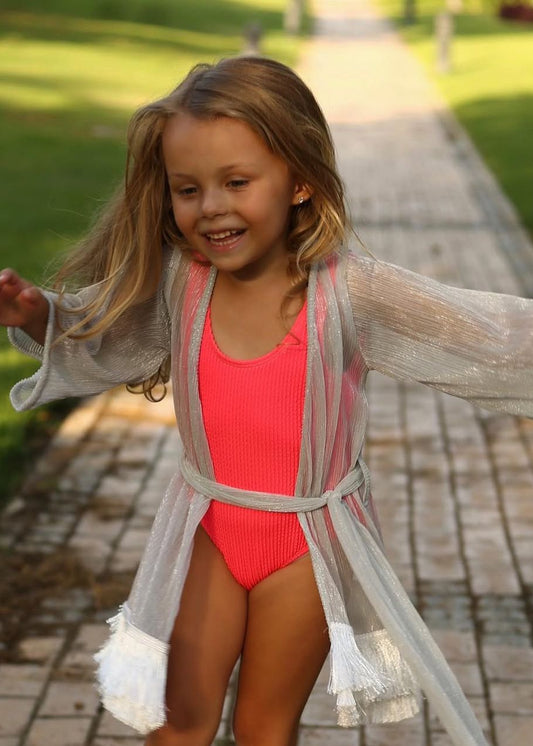 Young girl in red swimsuit and gray cover-up walking on a path in a garden.