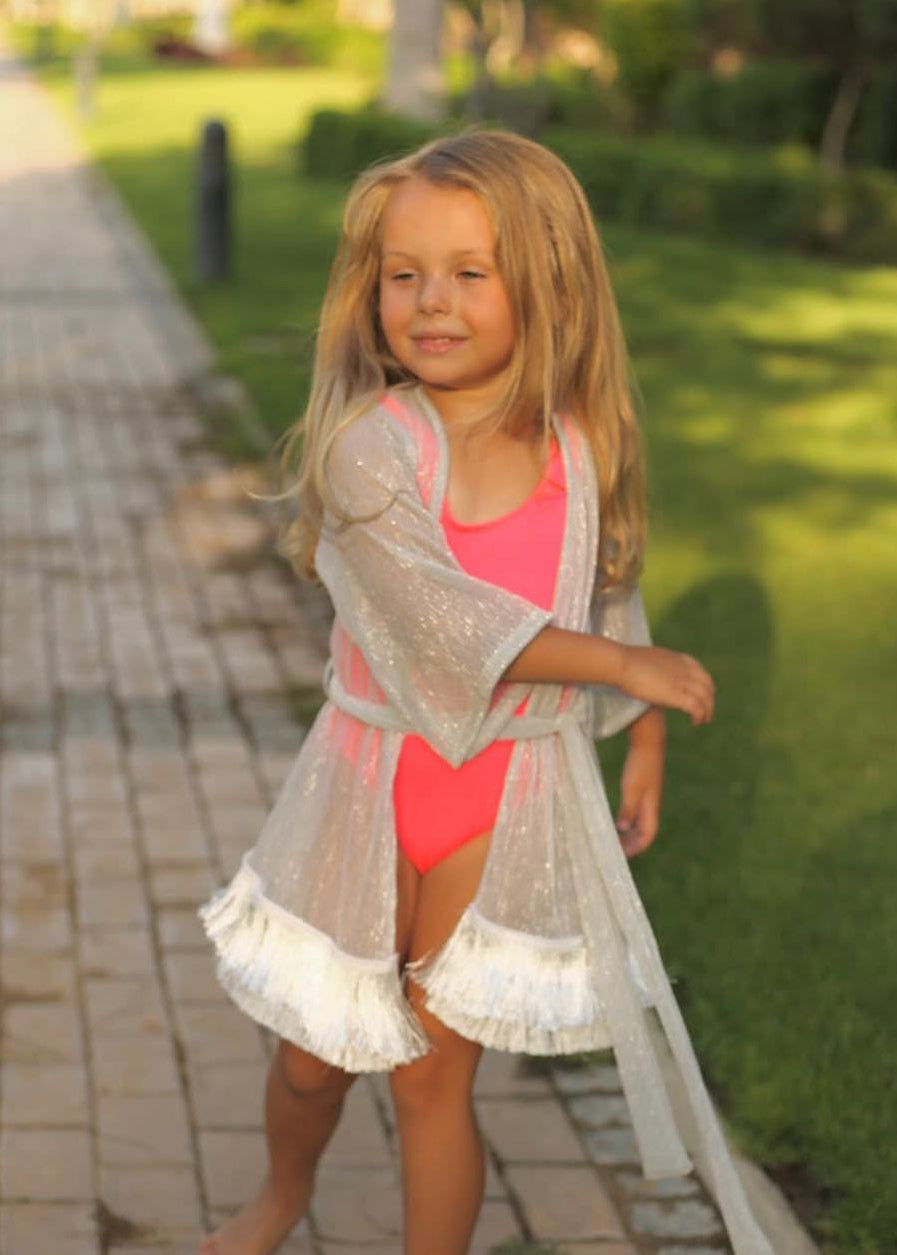 Young girl in a pink swimsuit and beige cover-up walking on a path in a park.