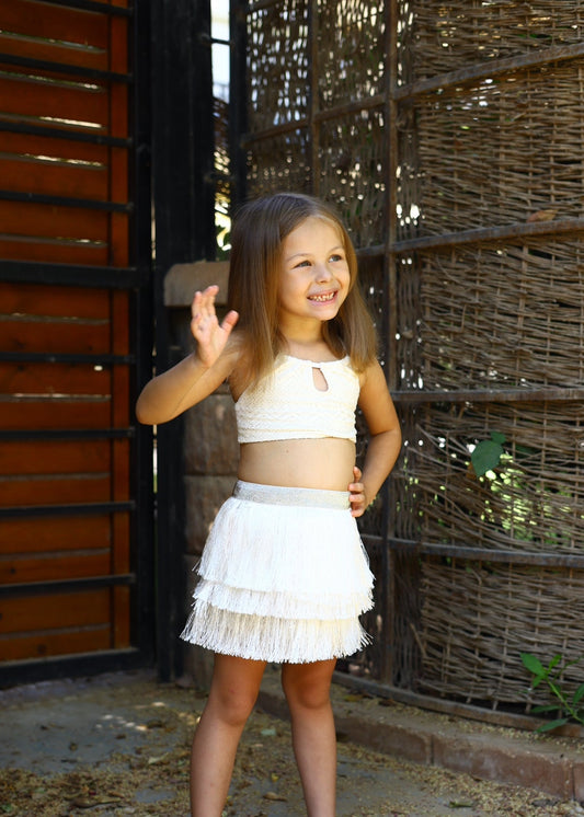 Young girl in a white outfit standing in front of a rustic wooden wall.