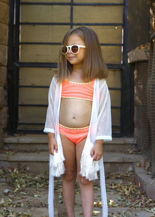Young girl in a red swimsuit and white cover-up standing outdoors.