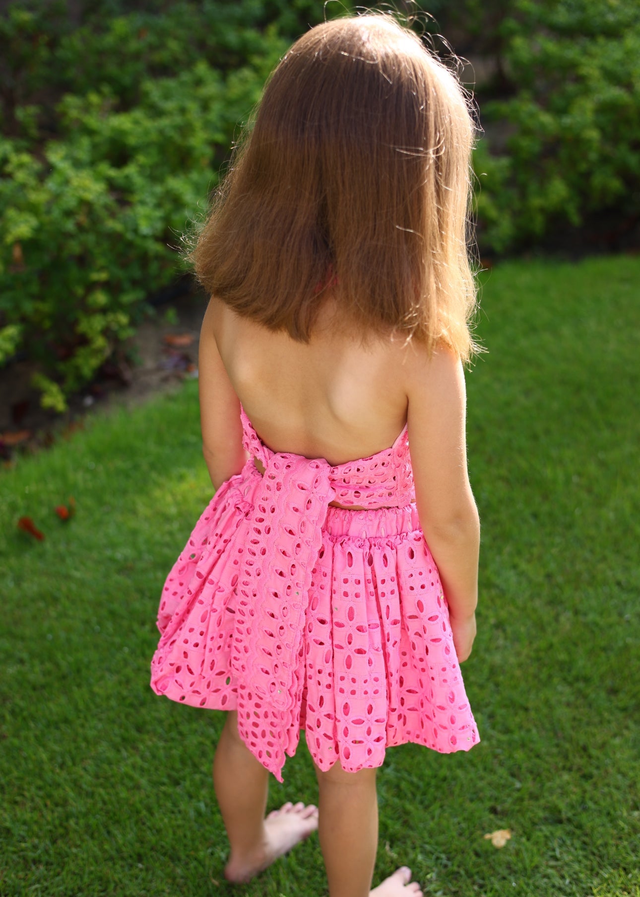 Child wearing a pink dress with a backless design, standing on grass.