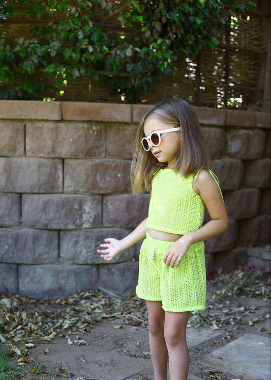 Young girl in a green outfit standing in front of a stone wall with foliage.