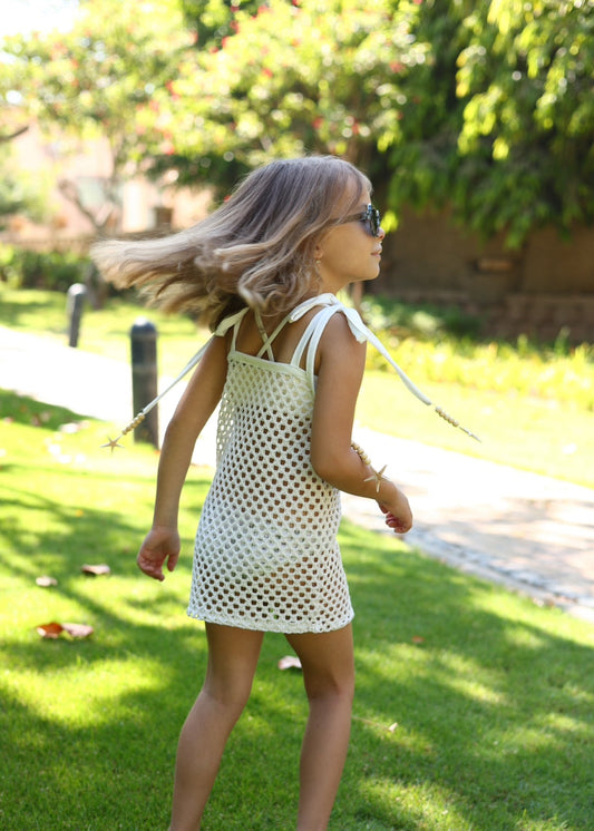Young girl in a white dress with a net pattern walking on grass.
