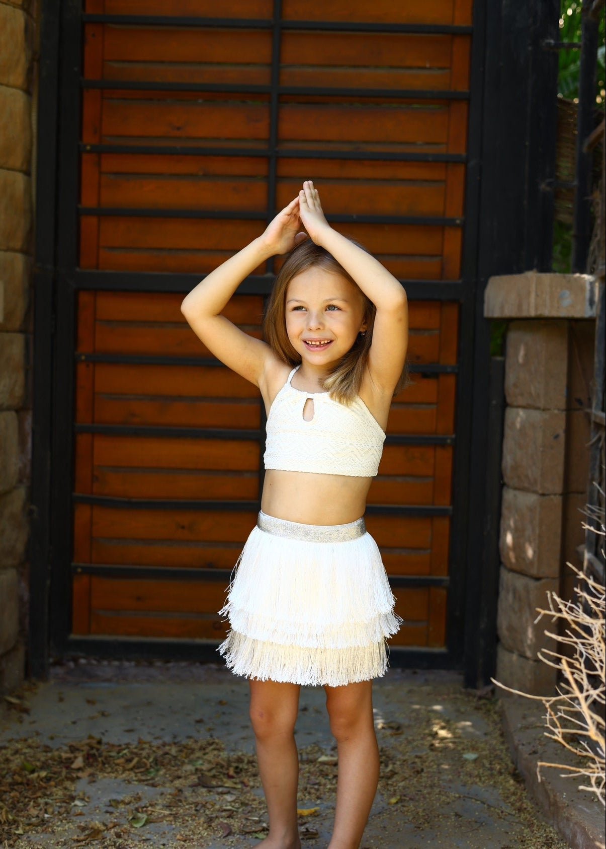 Young girl in a white outfit standing outdoors with a wooden door in the background
