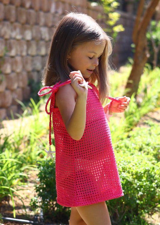 Young girl in a pink dress standing outdoors with greenery and a stone wall in the background