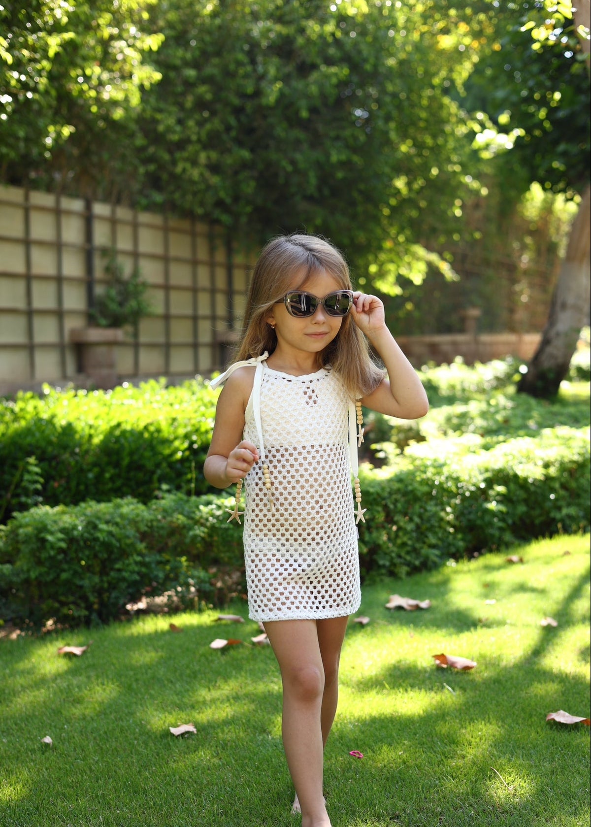 Young girl in a white dress and sunglasses standing in a garden.