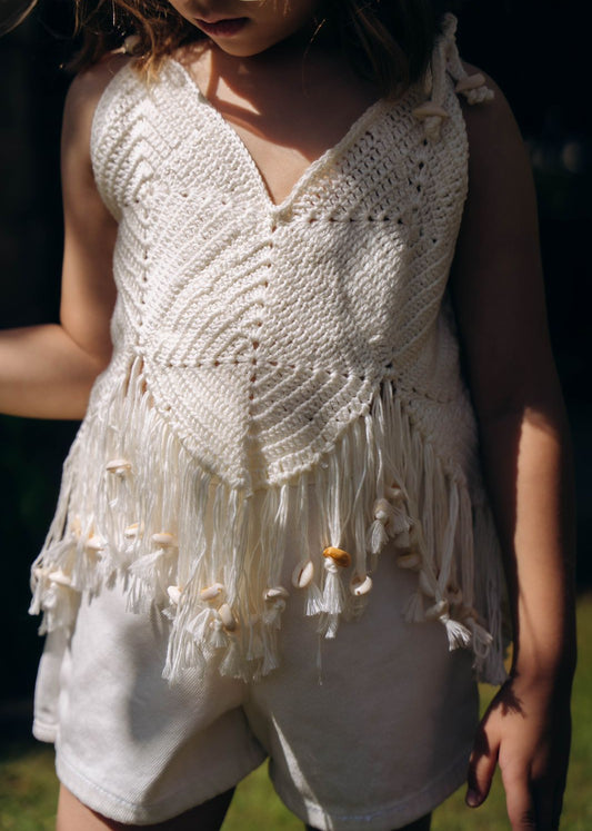 Child wearing a white crochet top with fringe and shorts outdoors