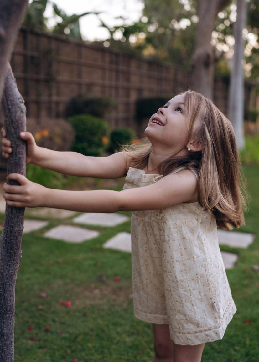 Young girl in a garden reaching up to touch an elephant's trunk.