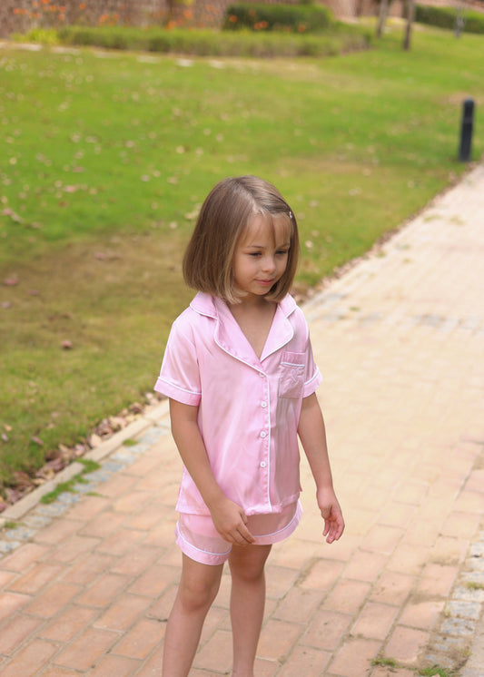 Young girl in a pink outfit standing on a paved path with grass in the background