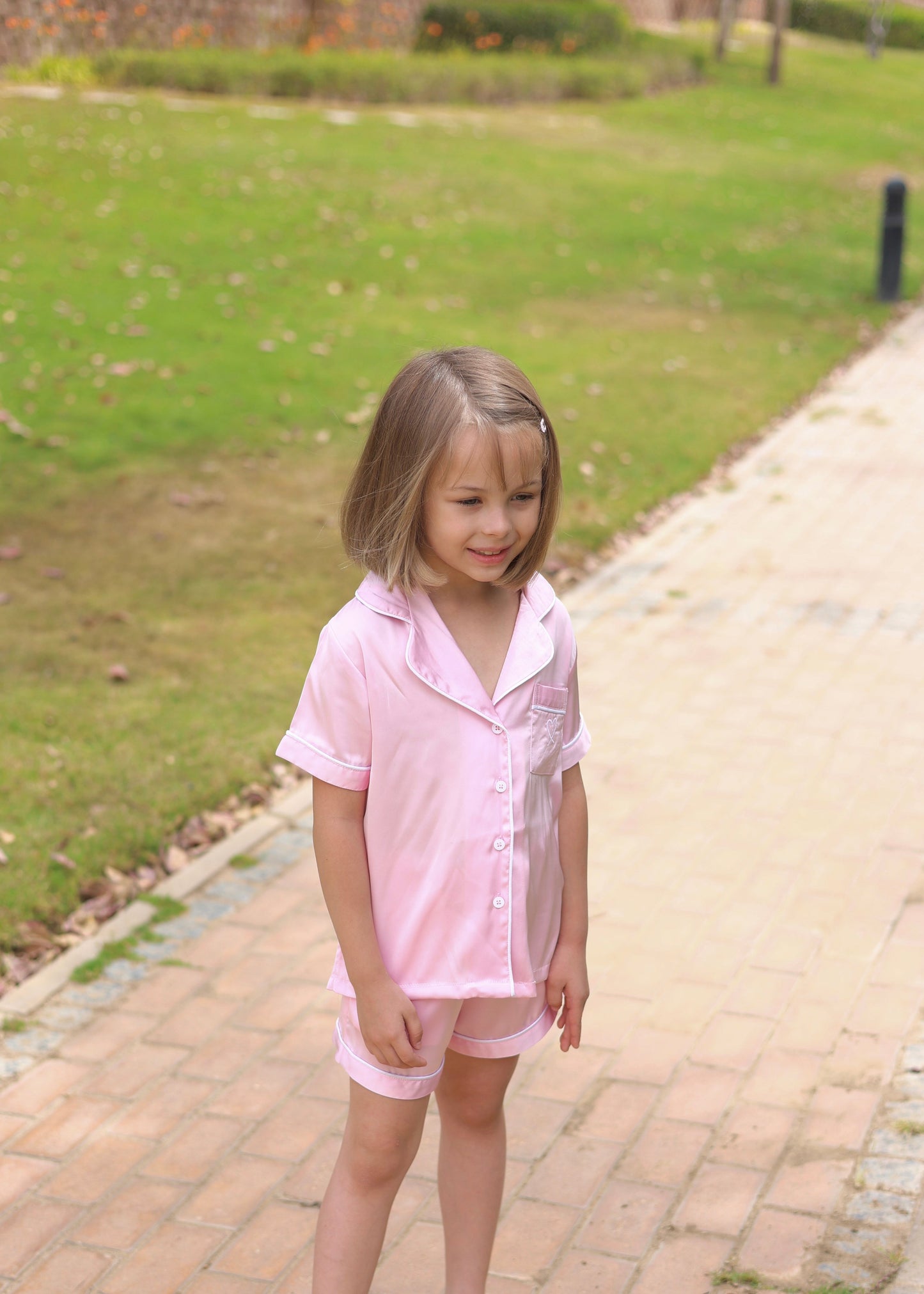 Young girl in a pink outfit standing on a paved path with grass in the background