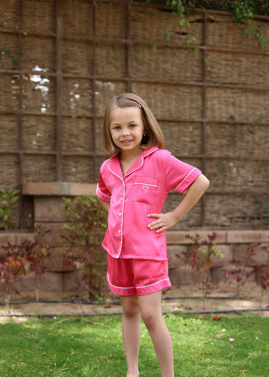 Young girl wearing a pink outfit standing outdoors with a woven wall background