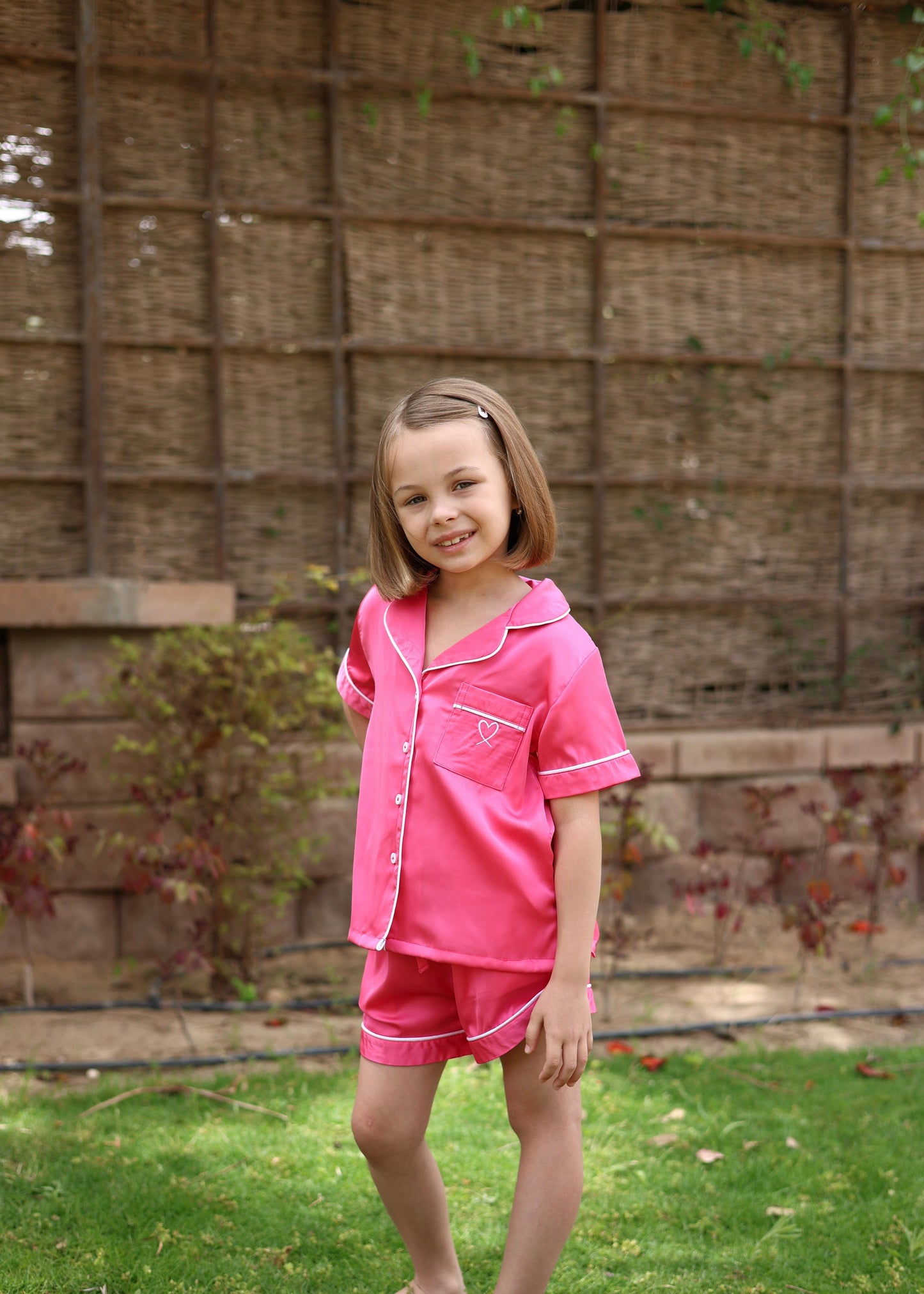 Young girl in pink pajamas standing in a garden with a woven wall background
