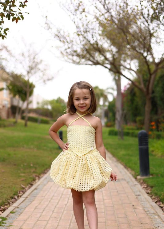 Young girl in a yellow dress standing on a path with trees and grass in the background