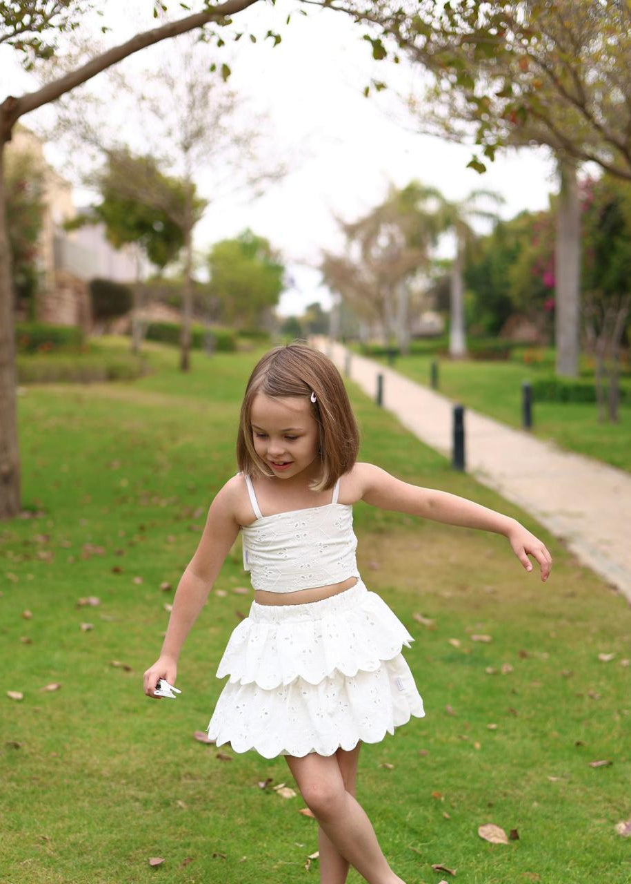 Young girl in a white dress standing on grass with trees and a path in the background