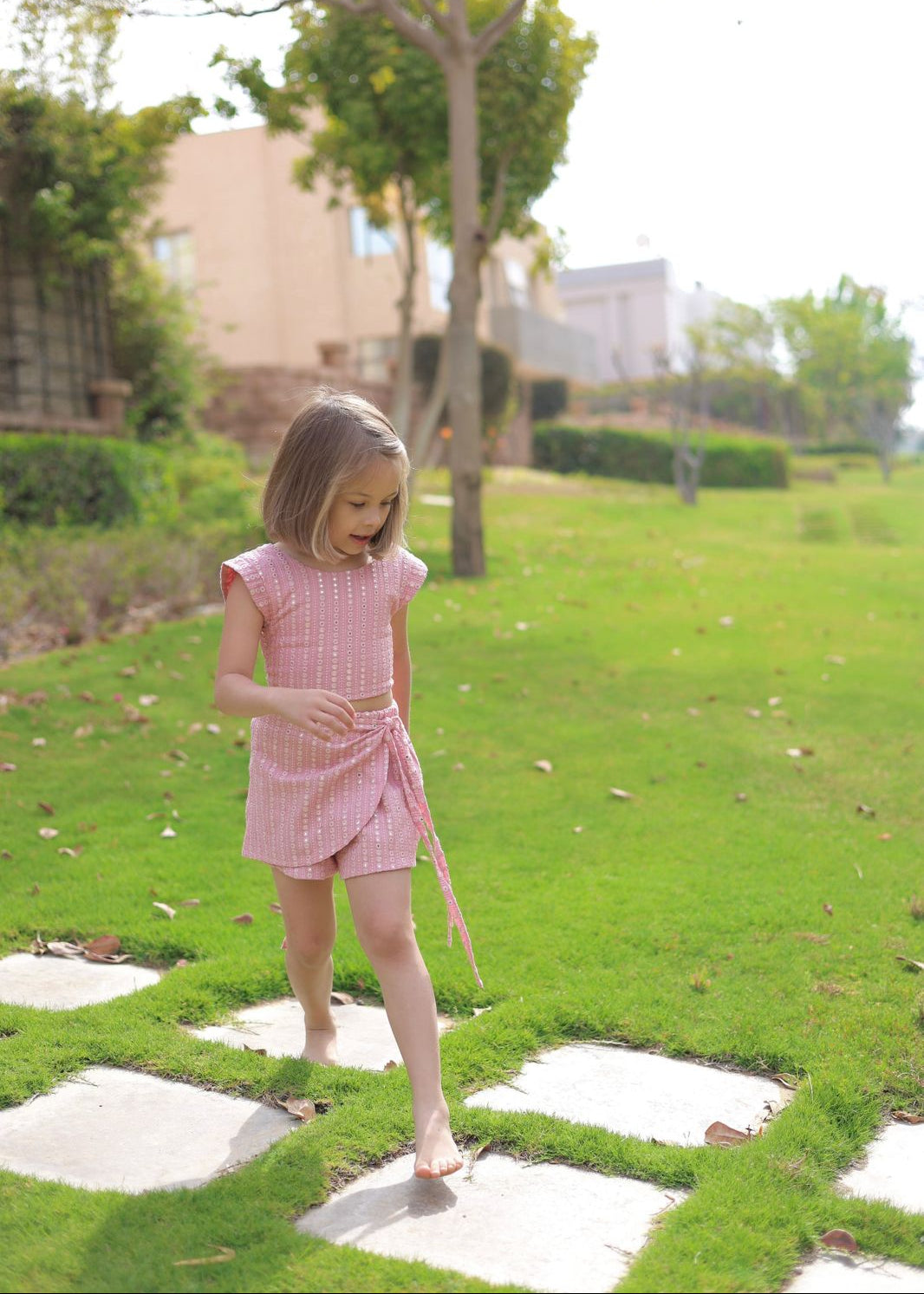Young girl in a pink dress standing on stone pathways in a garden.