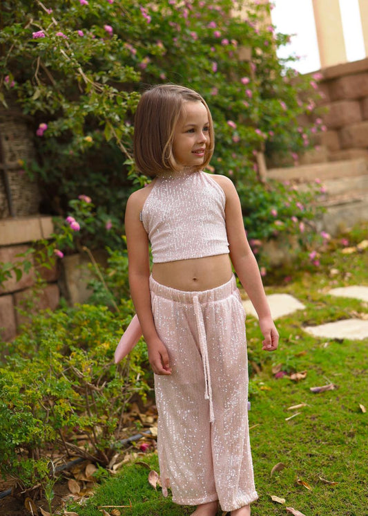 Young girl in a sparkly outfit standing outdoors with greenery and steps in the background