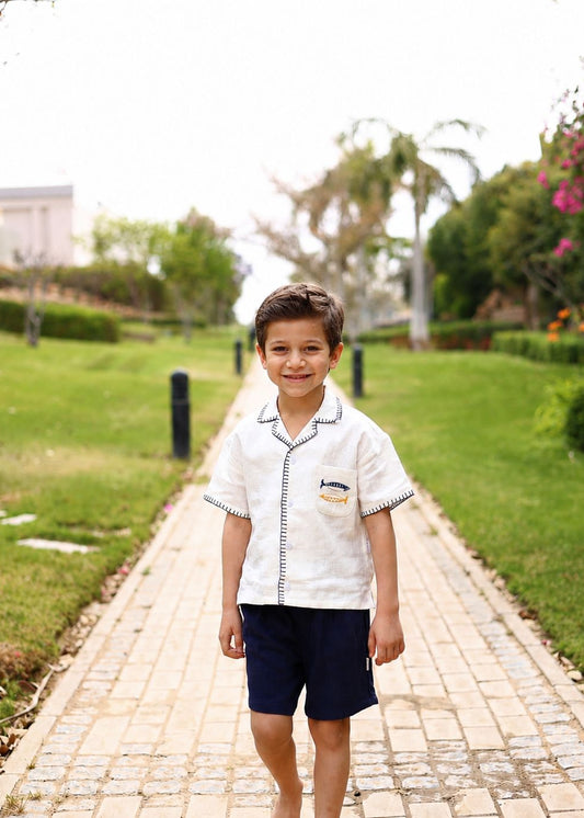 Child in a white shirt and navy shorts standing on a paved path in a park.