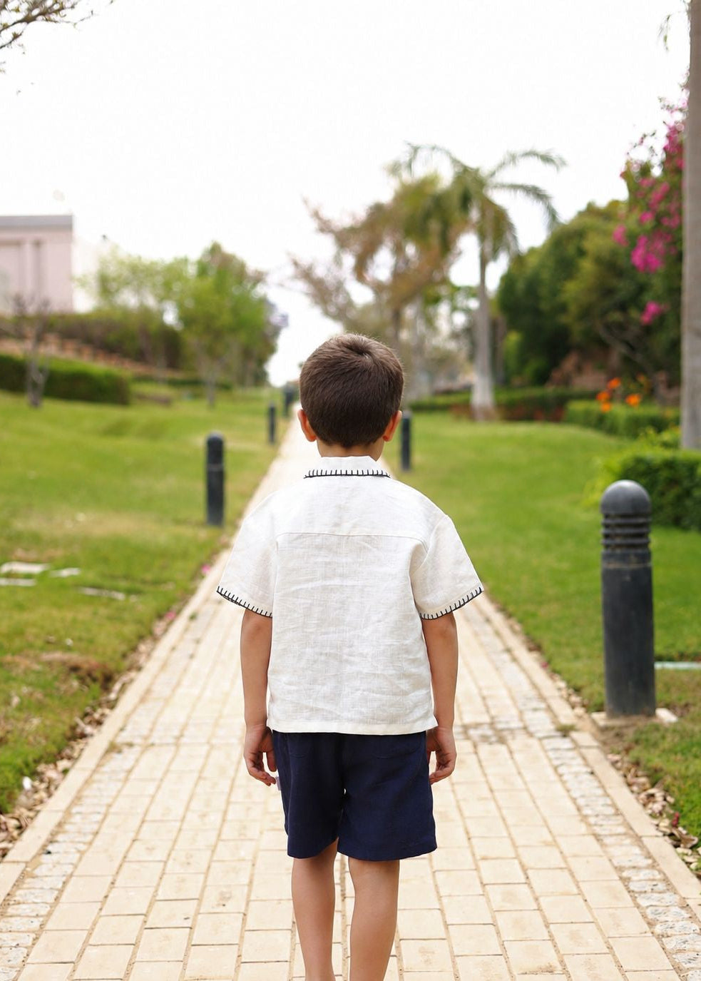 Child walking away on a paved path in a park with green grass and trees.