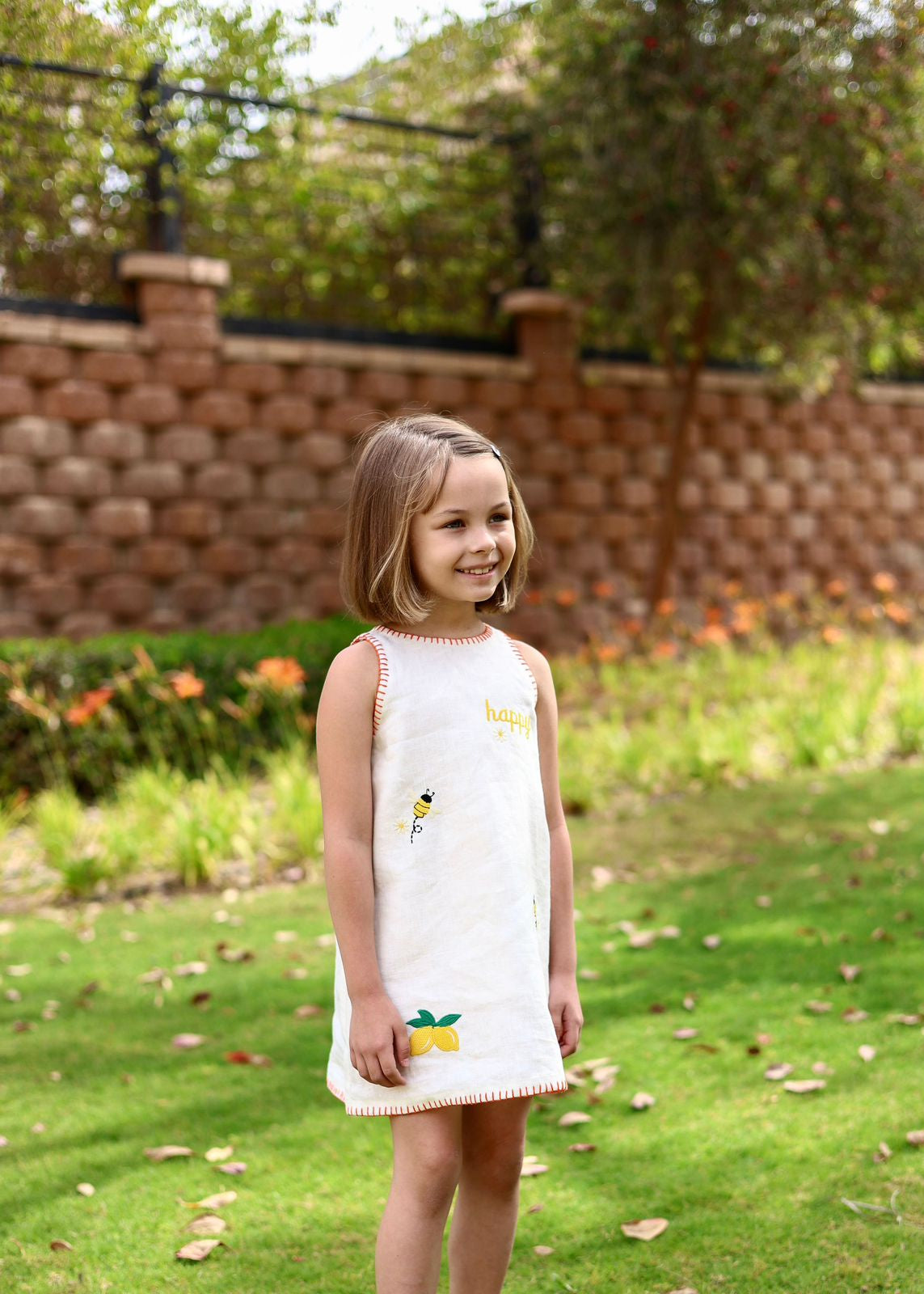 Young girl in a white dress with lemon design standing in a garden.