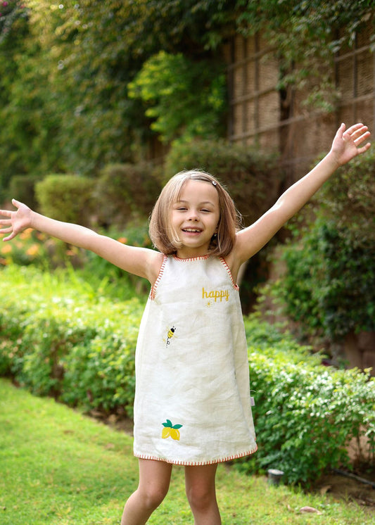 Child in a garden wearing a dress with 'happy' printed on it