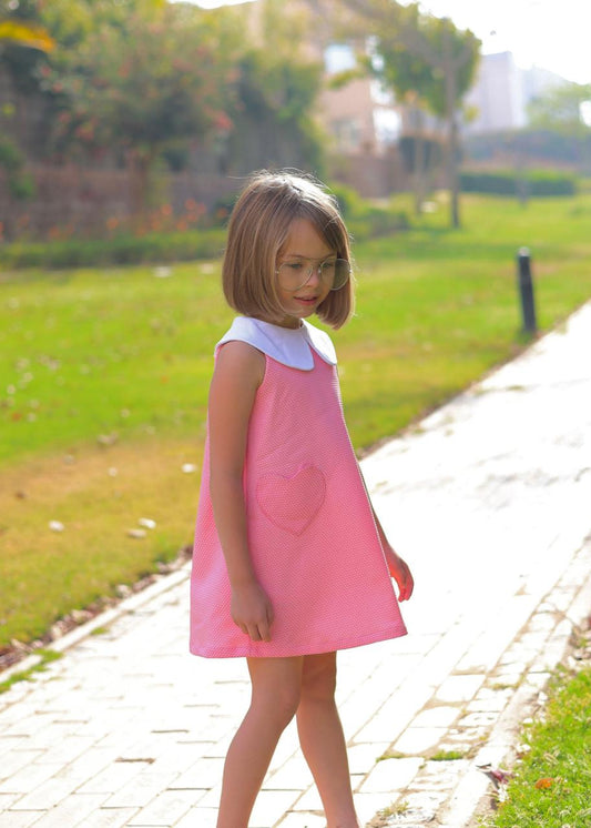 Young girl in a pink dress with a heart design standing on a path with greenery in the background