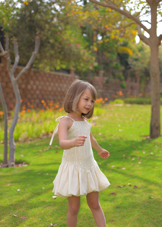 Young girl in a white dress standing in a park with trees and grass.