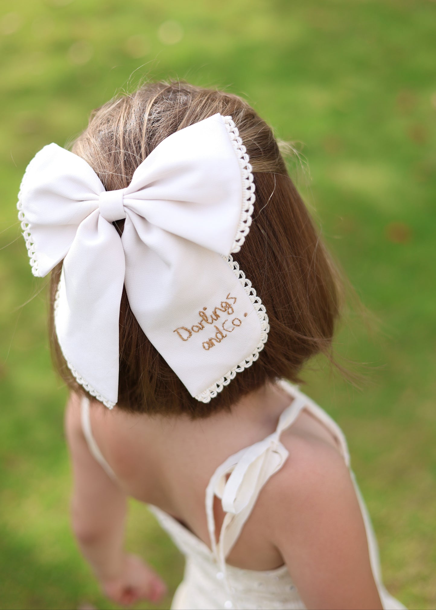Child with a large white bow in their hair against a green grass background