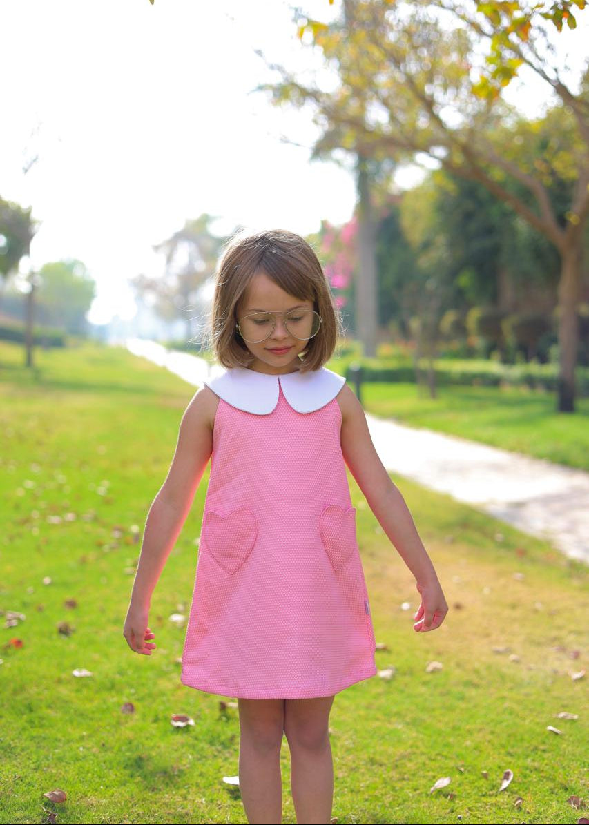 Young girl in a pink dress with a white collar standing in a park.